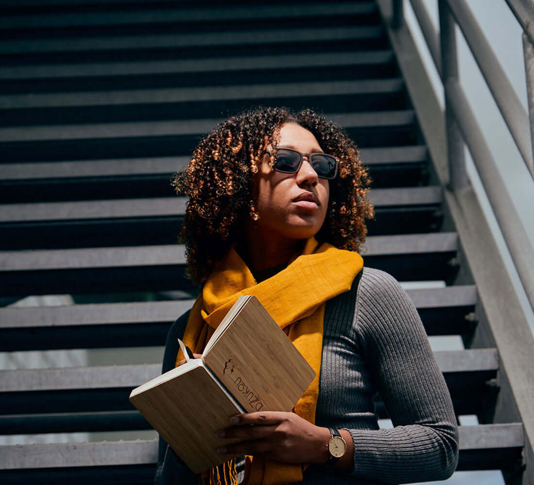 woman wrapped up in a mustard stole holding a notebook